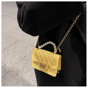 Detail of yellow mini silicone jelly bag with pearl handle and golden chain on black coat