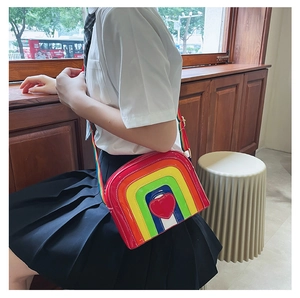 Rainbow crossbody bag with heart detail worn by a model in a cafe setting
