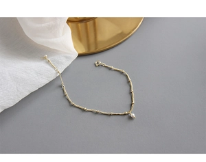 Detail of gold beaded chain bracelet with pearl pendant and spring clasp on silk background