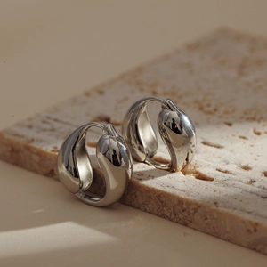 Polished silver teardrop hoop earrings displayed on a minimalist marble stone surface