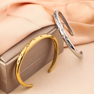 Close-up of gold and silver star engraved open bangles with zircon on satin fabric