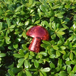 Close-up of a red mushroom disco ball ornament nestled in vibrant green garden shrubs