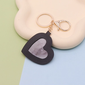 Macro detail of black PU leather heart keychain with mirror and gold metal ring on tray
