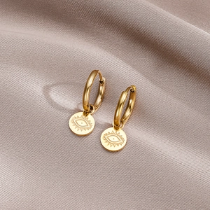 Polished gold evil eye hoop earrings with engraved pendants on silk background