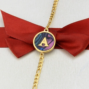 Macro detail of golden letter A pendant with abalone shell on a figaro chain