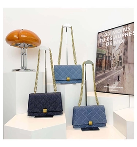 Close-up of denim quilted crossbody bags with gold chains on a white podium
