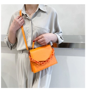 Detail of bright orange crossbody bag with chunky plastic chain on neutral outfit