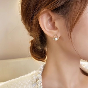 Close-up of elegant gold drop pearl earrings worn by a model in soft indoor light