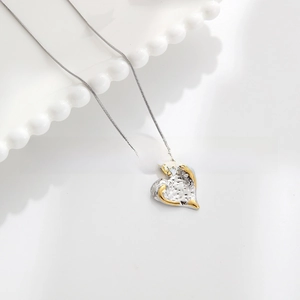 Detail of hammer textured heart pendant in gold and silver on fine snake chain