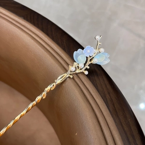 Close-up of golden hair pin with light blue translucent petals and white pearl accents