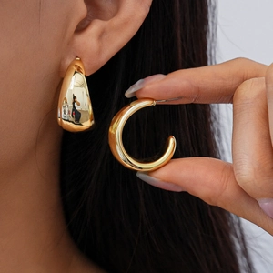 Close-up of golden wide C-shaped hoop earrings with polished finish on model and in hand