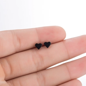 Macro shot of small black heart stud earrings held on a finger for size perspective