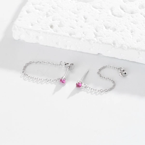 Macro detail of silver drop earrings featuring a sparkling pink zircon and fine link chain
