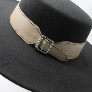 Gros plan du chapeau en laine noir avec bande en cuir beige et boucle en métal argenté