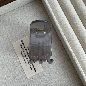 Close-up of a translucent smoky gray 5cm hair claw clip on a linen texture tray
