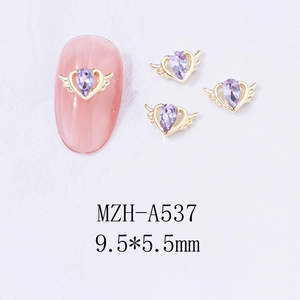 Detail of winged heart nail charm with purple teardrop gem and golden alloy base