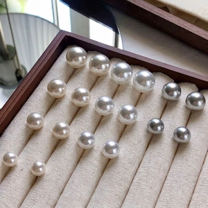 Elegant pearl stud earrings set in white, gold and grey displayed on a wooden tray