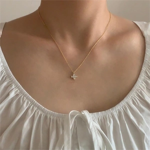 Close-up of a delicate gold cross necklace with zircon stones worn by a model