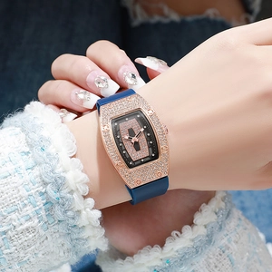 Detail of tonneau-shaped rose gold watch with crystal inlay and blue silicone strap