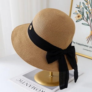 Detail of straw sun hat featuring a black ribbon bow and gold metal charm on a stand