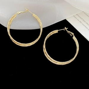 Detail of gold twisted circle earrings displayed on a monochrome background with soft fabric