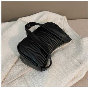 Close-up of black quilted PU leather shoulder bag with short handle on white fabric
