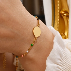 Close-up of gold chain bracelet with colorful beads and round pendant on wrist