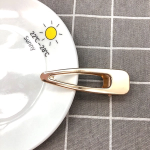 Detail of a minimalist gold hollow duckbill hair clip on a sun-patterned ceramic plate