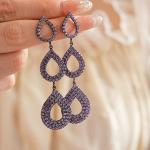 Macro detail of triple-layer purple teardrop earrings with crystal pavé and geometric fringe