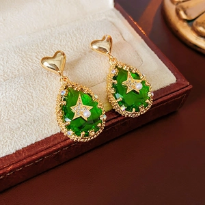 Close-up of gold heart earrings with green teardrop stones and pearl star in a box