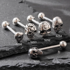 Five assorted skull head stainless steel tongue rings and studs on a black rock surface