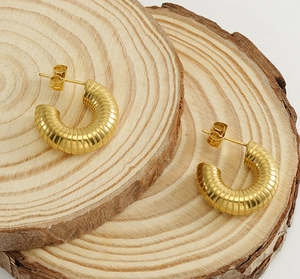 Close-up of gold U-shaped earrings with textured ridges on natural wood slices