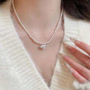Detail of a vintage pearl necklace with a blue rocking horse pendant on a white sweater