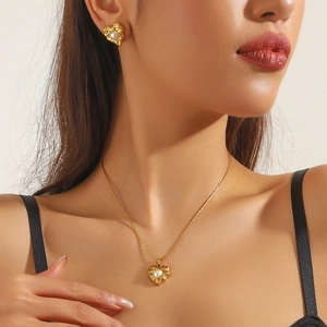 Model wearing gold heart-shaped pendant necklace and earrings set with white pearls