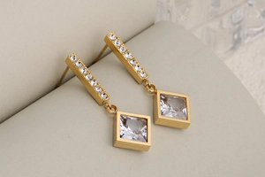 Macro detail of gold long drop earrings with square crystal pendants and zircon inlays
