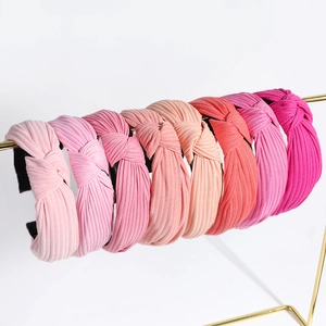Knitted knotted headbands in multiple shades of pink and coral on a gold display rack