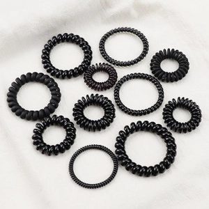 Détail d'un lot d'élastiques à cheveux spirale noirs de différentes tailles sur tissu beige