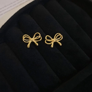 Close-up of golden bow-shaped stud earrings displayed in a black velvet jewelry box