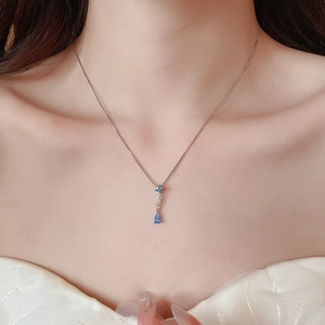 Detailed view of women silver necklace with a blue teardrop zircon pendant on a model
