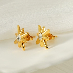 Macro shot of gold starburst stud earrings with central crystal on white silk