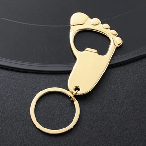 Polished gold foot-shaped bottle opener keychain on a textured black background