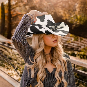 Detail of cow print western cowboy hat featuring a leather band with metal bull head ornament