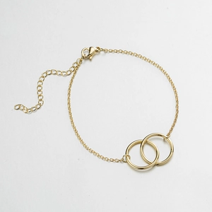 Detail view of double interlocking rings pendant with lobster clasp on a gold bracelet