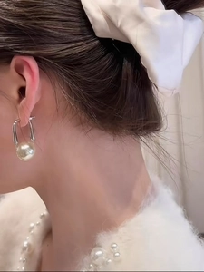 Close-up of minimalist silver U-shaped earrings with a single polished white pearl