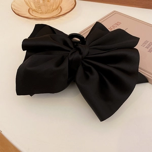 Grande pince à cheveux élégante avec nœud en satin noir posée sur une surface blanche