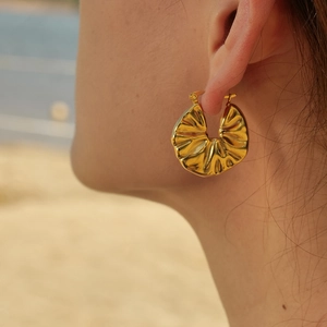 Primo piano di orecchino in acciaio al titanio oro 18K con design a pieghe