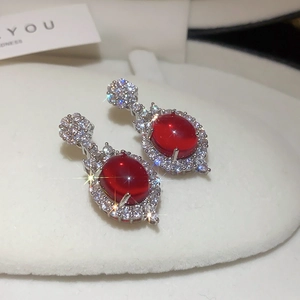 Close-up of vintage silver earrings featuring a red oval gemstone with zircon halo