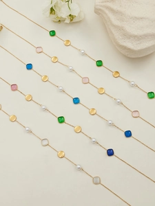 Detail of 18k gold-plated necklace with colorful resin beads and faux pearls on a beige surface