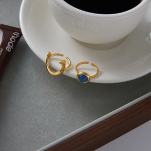Gold nail-shaped wrap ring and blue stone band set on elegant white porcelain cup edge