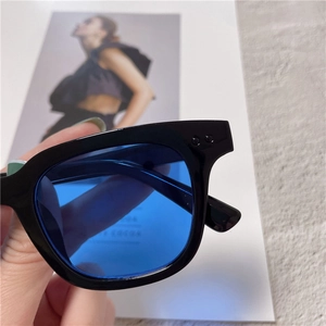 Close-up of black square frame sunglasses featuring transparent blue lenses and rivet detail